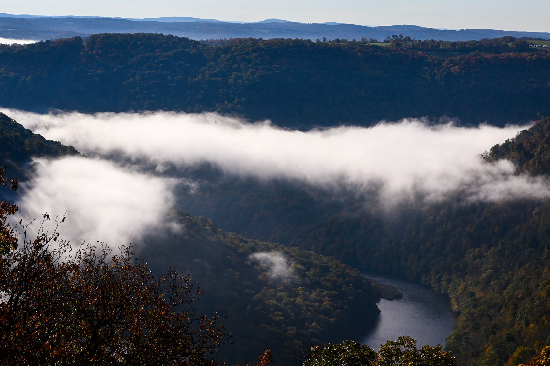 A river flowing through a mountainous valley at Cooper's Rock National Forest. Fog distills overhead.