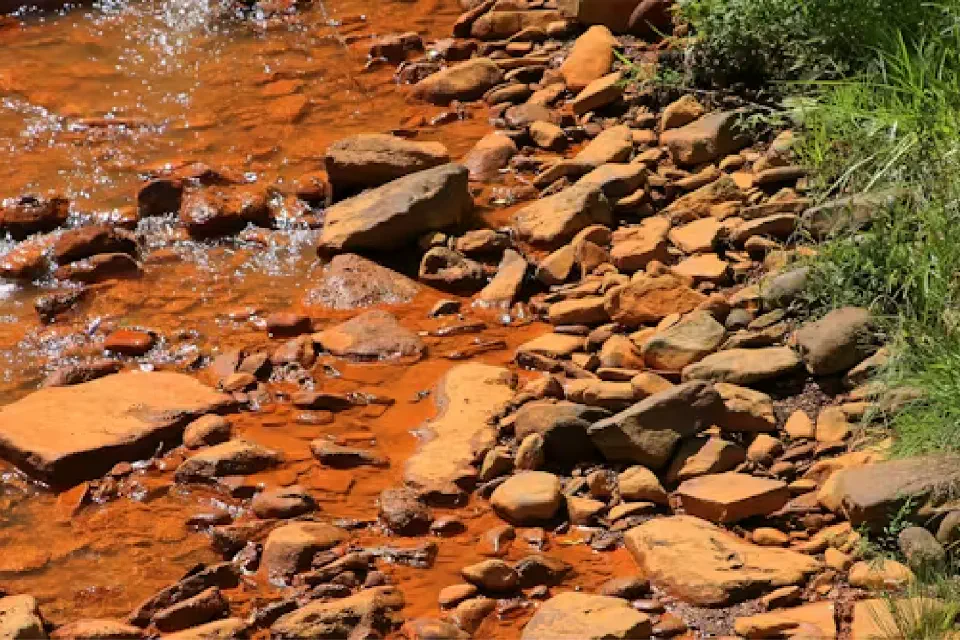 A riverbed of red rocks and water.